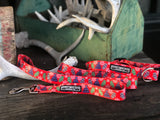 Red winter-themed Lucky Love Dog collar and leash set with mitten and hat pattern displayed on rustic wood with antler decor.