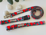 Red poinsettia-themed Lucky Love Dog collar and leash set displayed with smooth decorative stones and greenery.