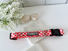 Red gingham dog collar with bumblebees, displayed on marble with white stones and flowers.
