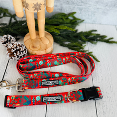 Red Christmas dog collar and leash set with a Nutcracker pattern, displayed on wood with pine cones and greenery.
