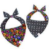 Two pet bandanas shown on a white background, each with a bow at the top and a triangular front panel. One bandana has a dark gray and white polka dot design with a multicolor floral print on the front; the other has a dark gray and white polka dot design with a multicolor floral print on the reverse side.
