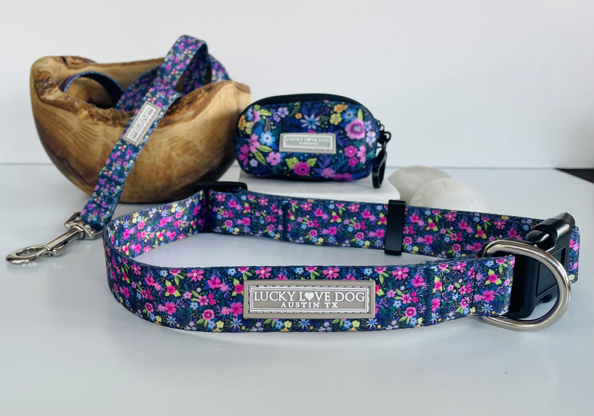 Purple floral dog collar set by Lucky Love Dog featuring a matching leash in a wooden bowl and a small accessory pouch.