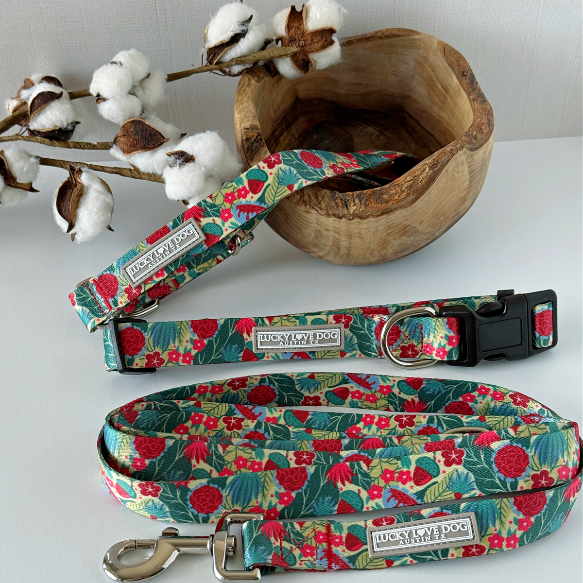 Floral-patterned dog collar and leash set on a white surface with cotton branches in the background.