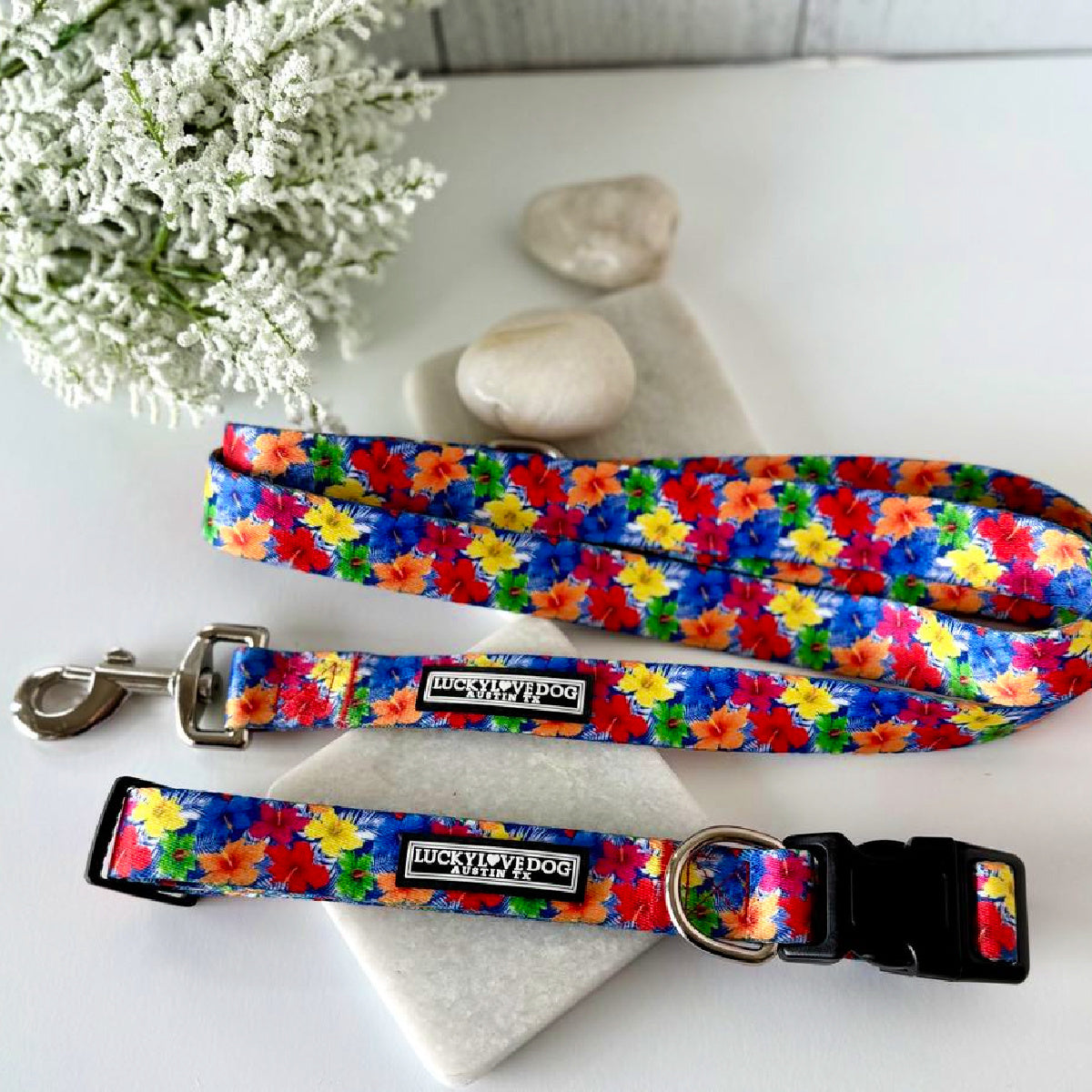 Tropical hibiscus patterned dog collar and leash set displayed on white stones with white flowers.