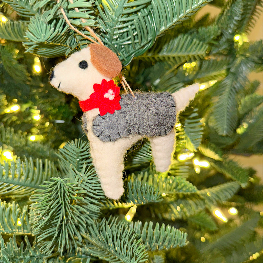 Felt terrier dog Christmas ornament with a grey sweater and red flower hanging on a pine tree