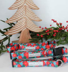 Red poinsettia-themed Lucky Love Dog collars displayed with festive greenery and wooden Christmas décor.