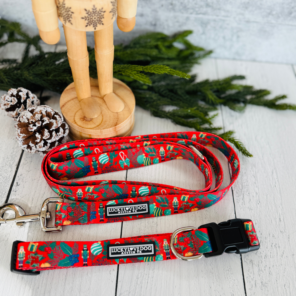 Red Christmas dog collar and leash set with a Nutcracker pattern, displayed on wood with pine cones and greenery.