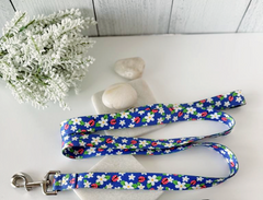 Blue dog leash with white daisies and ladybugs, displayed on white stones and flowers.